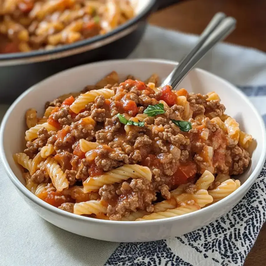 Pasta stacked with saucy beef, plus a basil leaf on top.