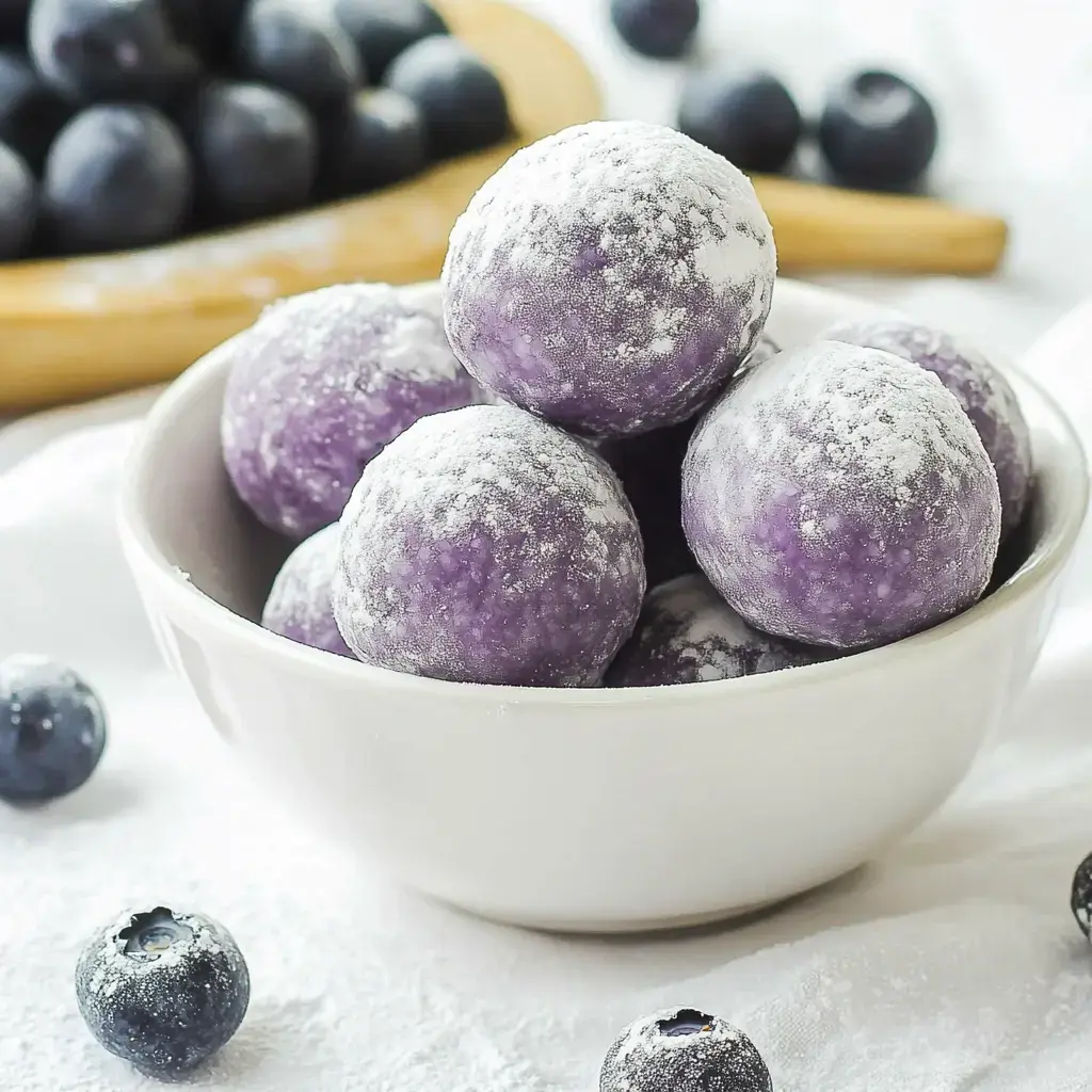 A bowl with powdery purple candies on a bright surface, with a few blueberries around.