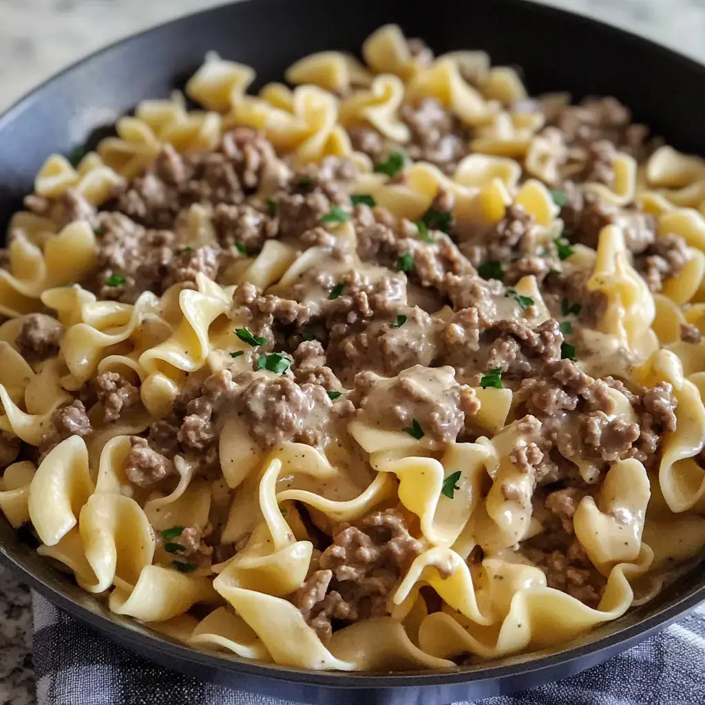 Egg noodles and ground beef in a creamy sauce, topped with parsley in a skillet.