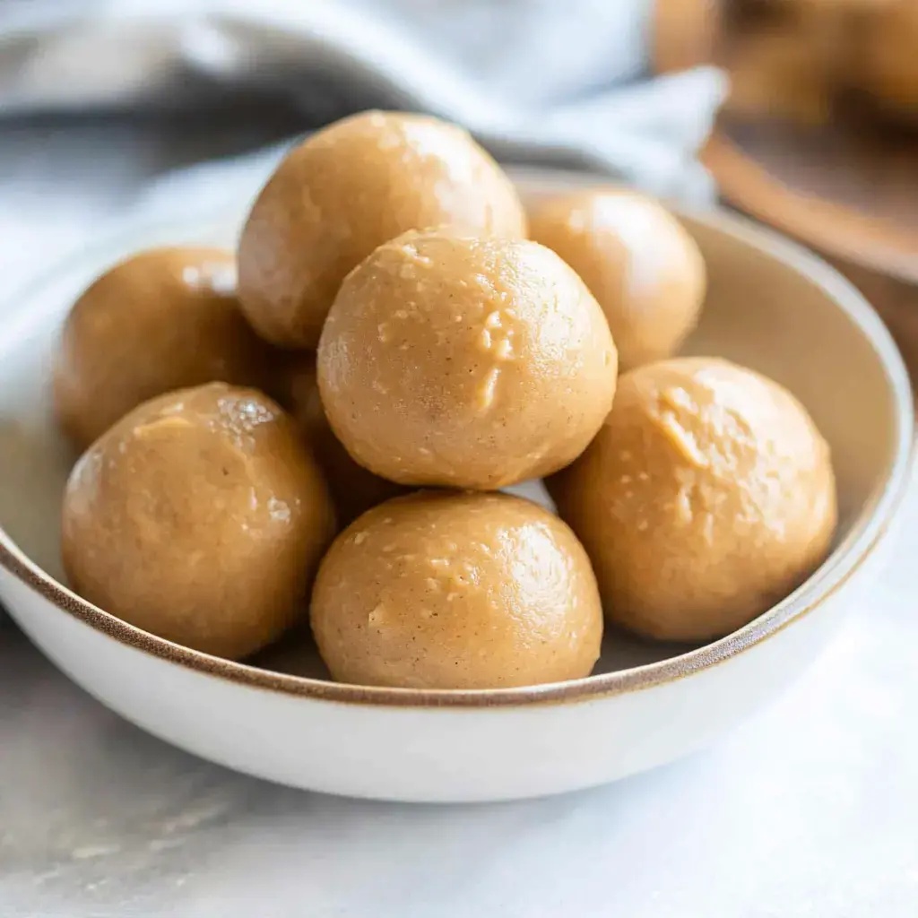 A bowl filled with round peanut butter bites sitting on a textured surface.