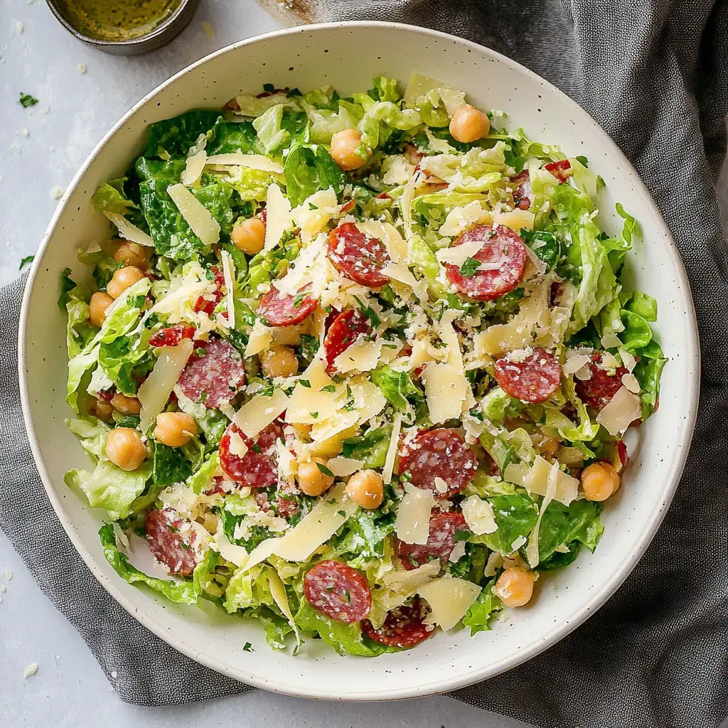 A fresh bowl of chopped romaine, salami slices, grated cheese, and chickpeas topped with herbs.