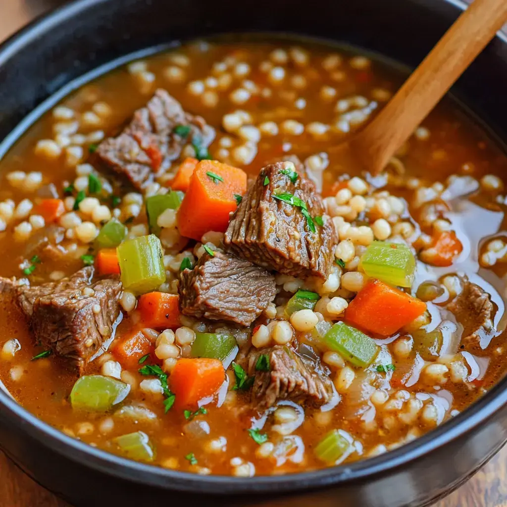 A mouthwatering beef barley soup showing tender meat, veggies like carrots and celery, plus fresh parsley garnish in a black bowl.