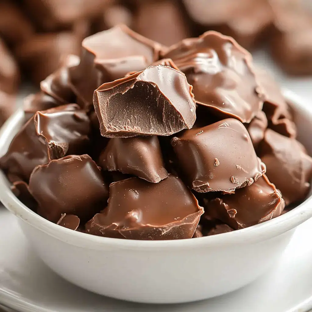 A white bowl showing chunks of velvety chocolate, with some pieces slightly cracked.
