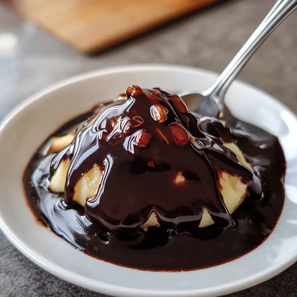 Vanilla ice cream with dark chocolate drizzle and sprinkled nuts in a white bowl.