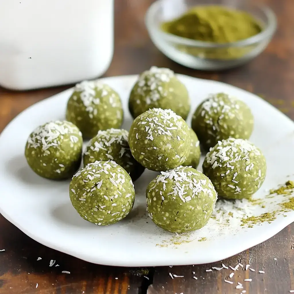 Matcha-flavored balls covered in coconut sit on a plate, with a sprinkle of vibrant green powder nearby for garnish.