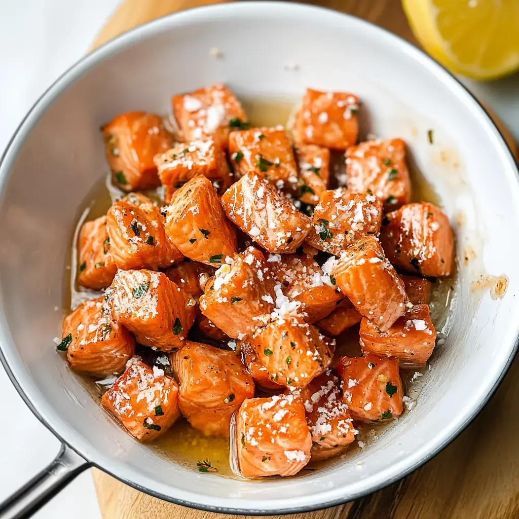 Crispy cooked salmon cubes in a bowl, sprinkled with herbs and cheese, sitting in a light dressing, with a lemon on the side.