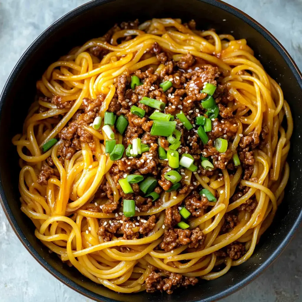 Bowl of spaghetti noodles, sautéed ground beef, and a scatter of green onion and sesame seeds in close detail.