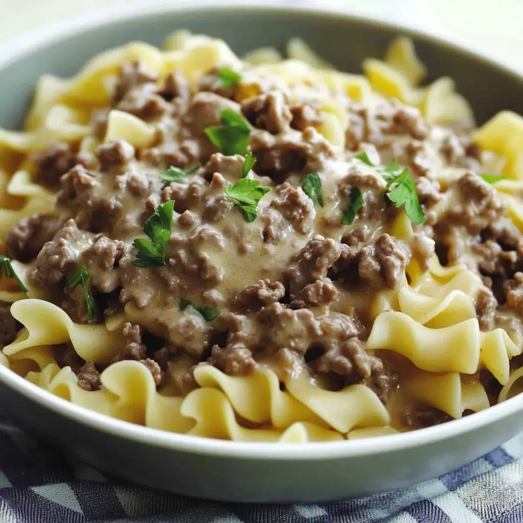 Egg noodles covered in creamy beef with a bit of parsley on top in a bowl.