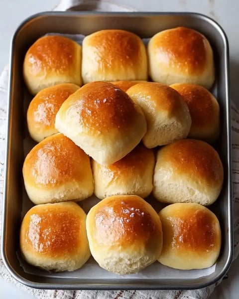 Golden rolls in a pan, one stacked on top of the rest.